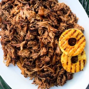 A white plate filled with Hawaiian pulled pork, served with two grilled pineapple rings on the side. Perfect for making pulled pork Hawaiian roll sliders or enjoying as a classic dish.