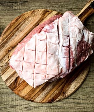 Raw pork roast with scored fat, placed on a round wooden cutting board against a wood-grain background.