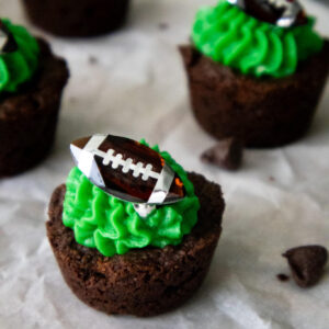 Close-up of a two-bite brownie topped with green buttercream icing and a football ring decoration.