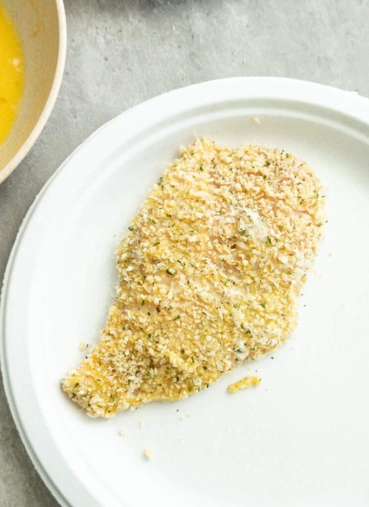 a chicken breast coated in breadcrumbs in preparation for frying