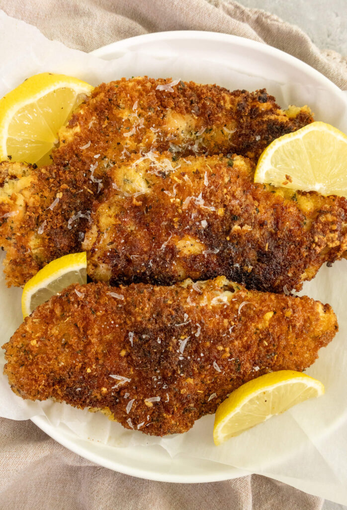 crispy chicken cutlets on a plate with lemon wedges 