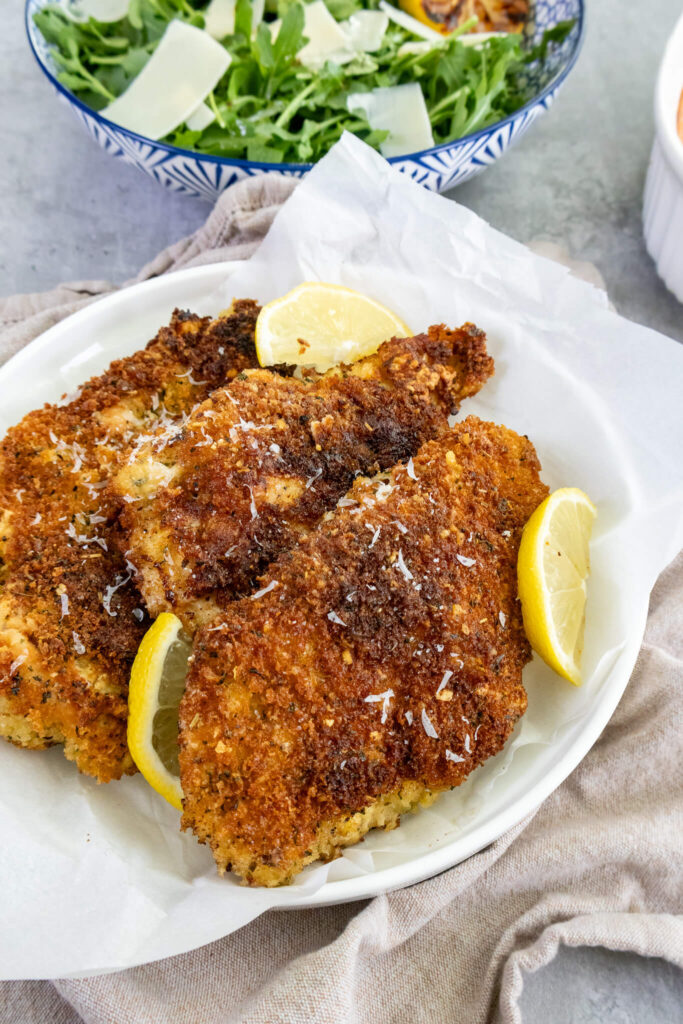 crispy chicken cutlets on a plate with lemon wedges 