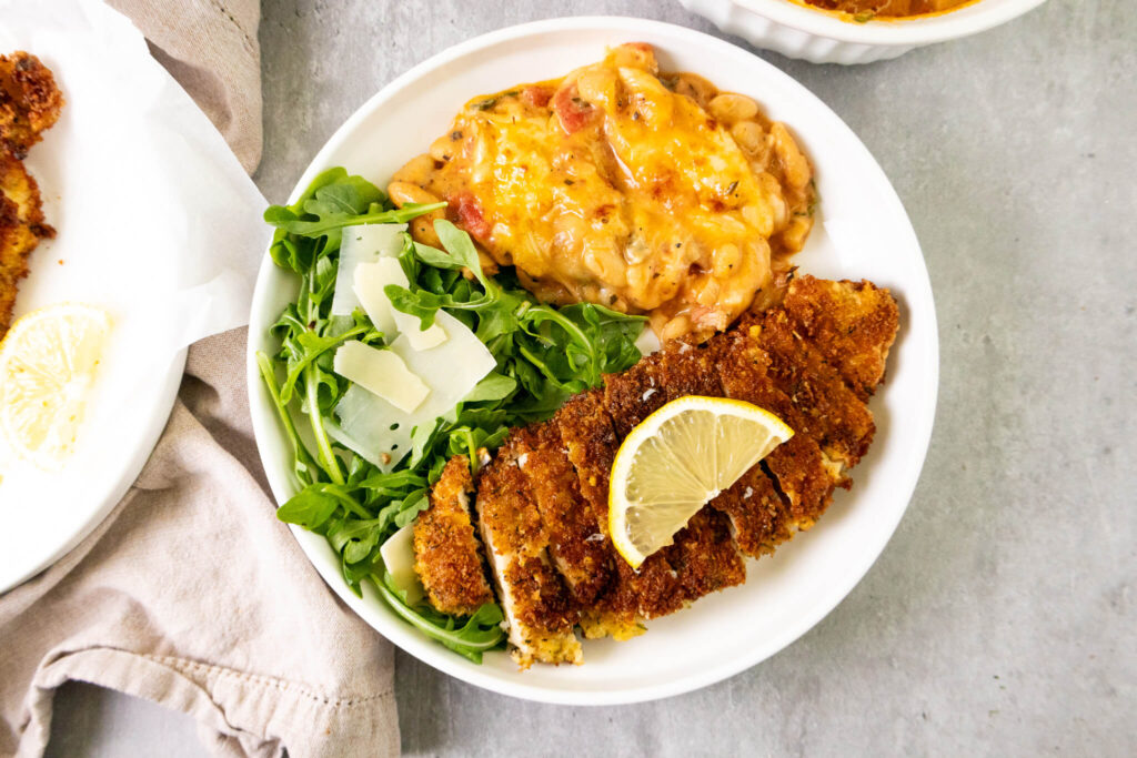 crispy chicken cutlet on a dinner plate served with baked beans and a salad