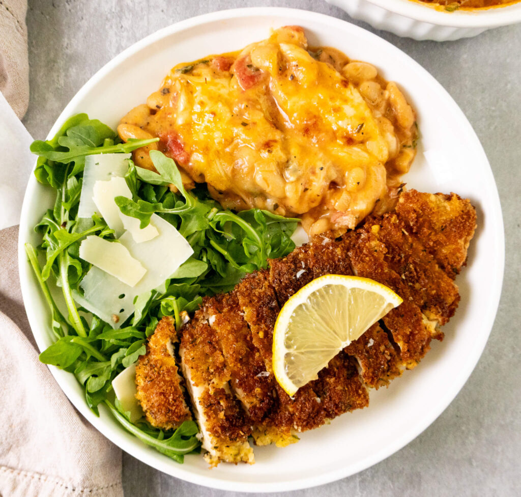 a serving suggestion of crispy chicken cutlets, baked cannellini beans, and parmesan and lemon arugula salad