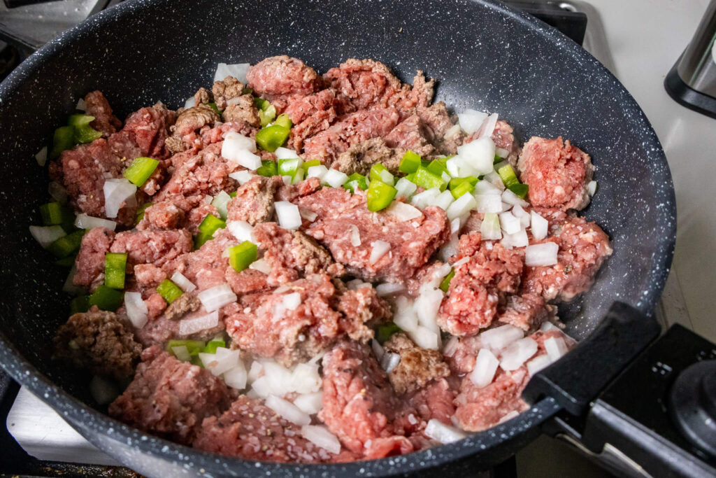 Ground beef, green bell peppers, and onions frying in a pan. 