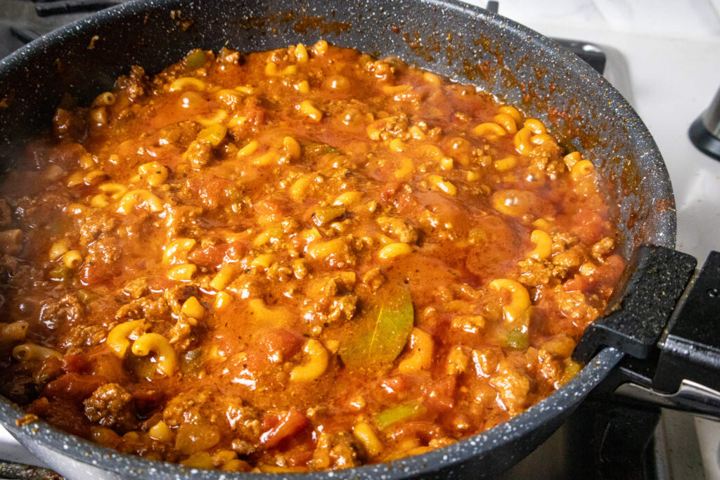 Beef, macaroni noodles, and tomato sauce cooking on the stove. 