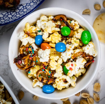 Photo of game day trail mix featuring popcorn, peanut M&Ms, chocolate-covered pretzels, Chex cereal, and colorful sprinkles, all mixed together in a large bowl.