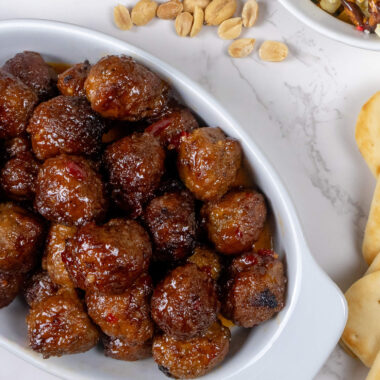 Close-up of sweet and spicy crockpot party meatballs, glistening with a rich, sticky glaze, served on a white platter with toothpicks for easy grabbing.