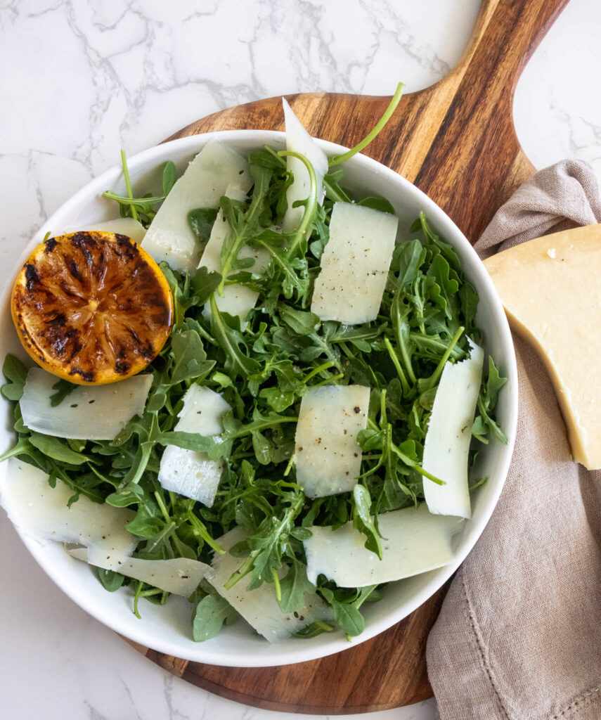 parmesan and lemon arugula salad on a cutting board with a wedge of parmesan alongside