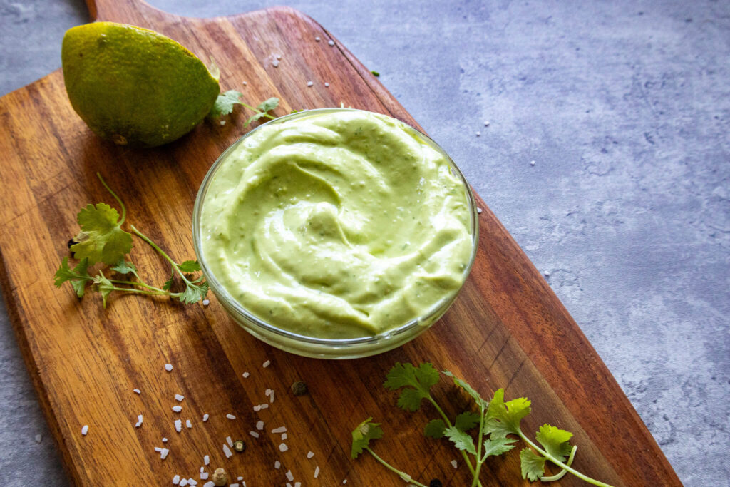 avocado crema in a bowl on top of a wooden cutting board 