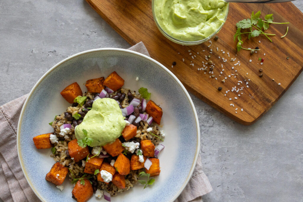 sweet potato and black bean quinoa bowl with avocado crema, queso fresco, cilantro, and red onion