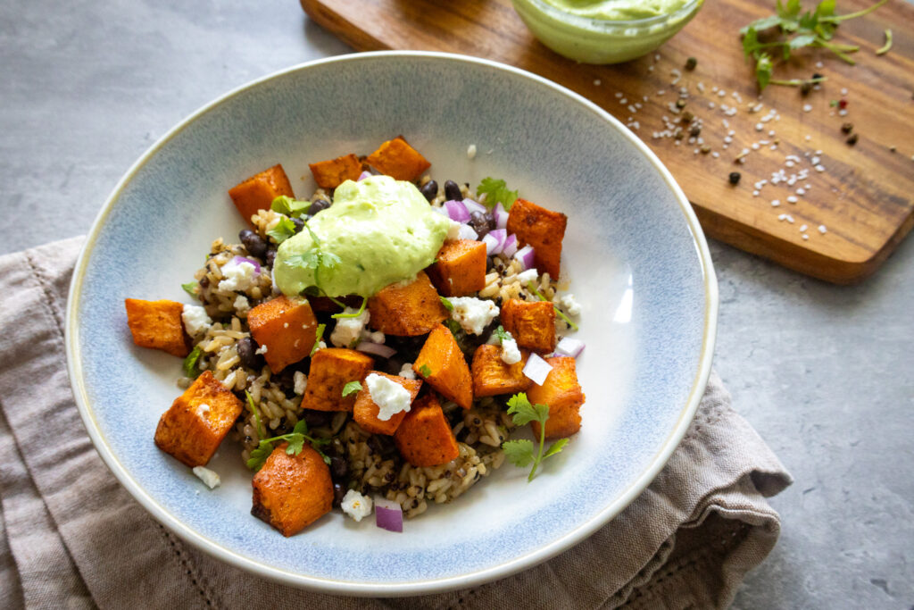 sweet potato and black bean quinoa bowl with avocado crema, queso fresco, cilantro, and red onion