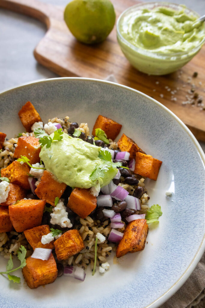 sweet potato and black bean quinoa bowl with avocado crema, queso fresco, cilantro, and red onion