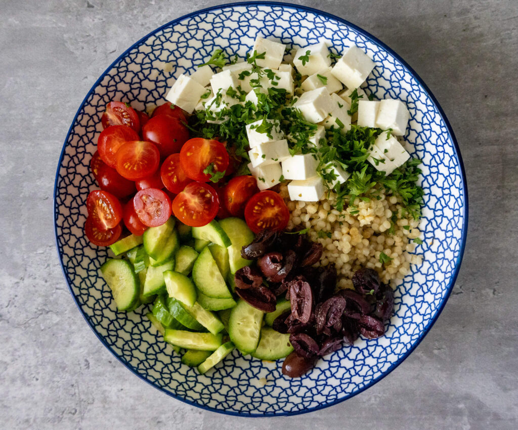 sliced cucumbers, cherry tomatoes, kalamata olives, feta cheese, parsley, and feta cheese in a blue bowl