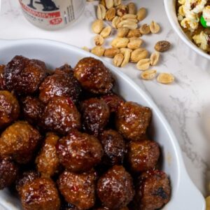 Close-up of sweet and spicy crockpot party meatballs, glistening with a rich, sticky glaze, served on a white platter with toothpicks for easy grabbing