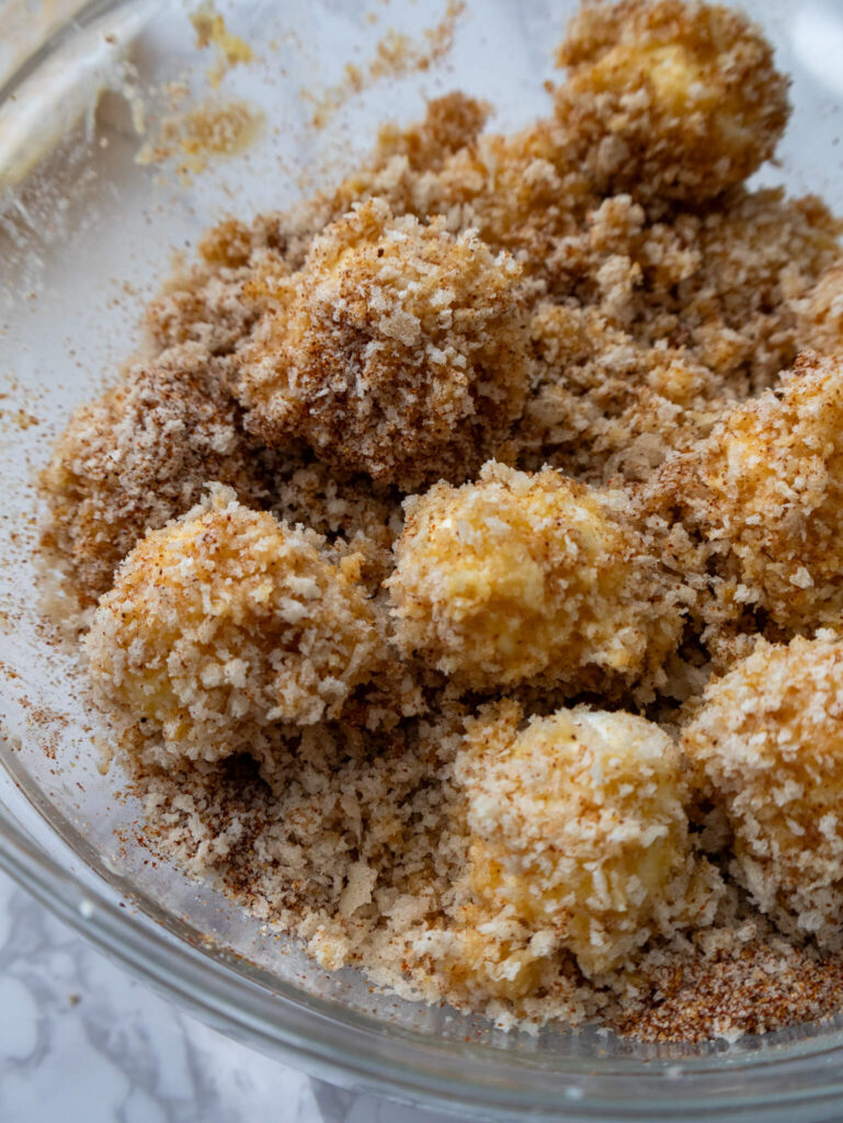 Mozzarella balls coated in egg and seasoned panko breadcrumbs, prepared for frying. 