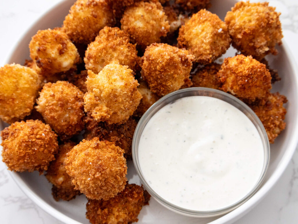 A round serving platter with crispy Nashville Hot Mozzarella Bites and ranch dipping sauce. 