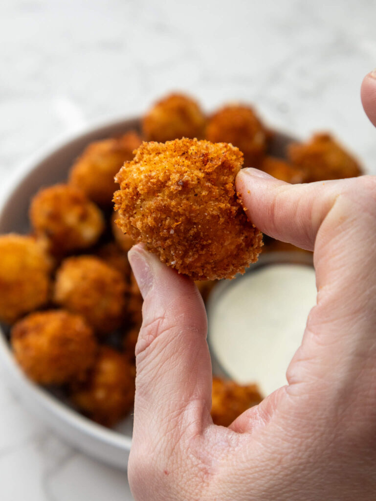 A round, crispy Nashville Hot Mozzarella bite with the serving plate and dressing i the background. 