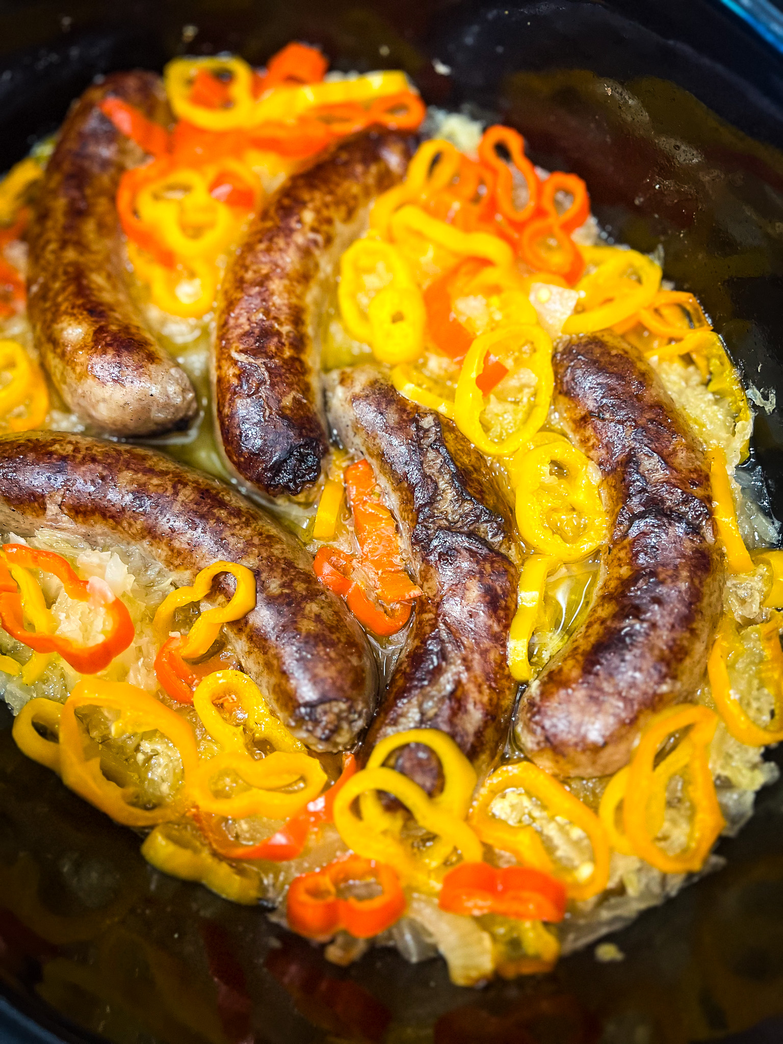 Sausages cooked in a slow cooker with sliced yellow and red bell peppers on a bed of onions. The sausages are browned, and the colorful peppers add a vibrant touch to the dish.