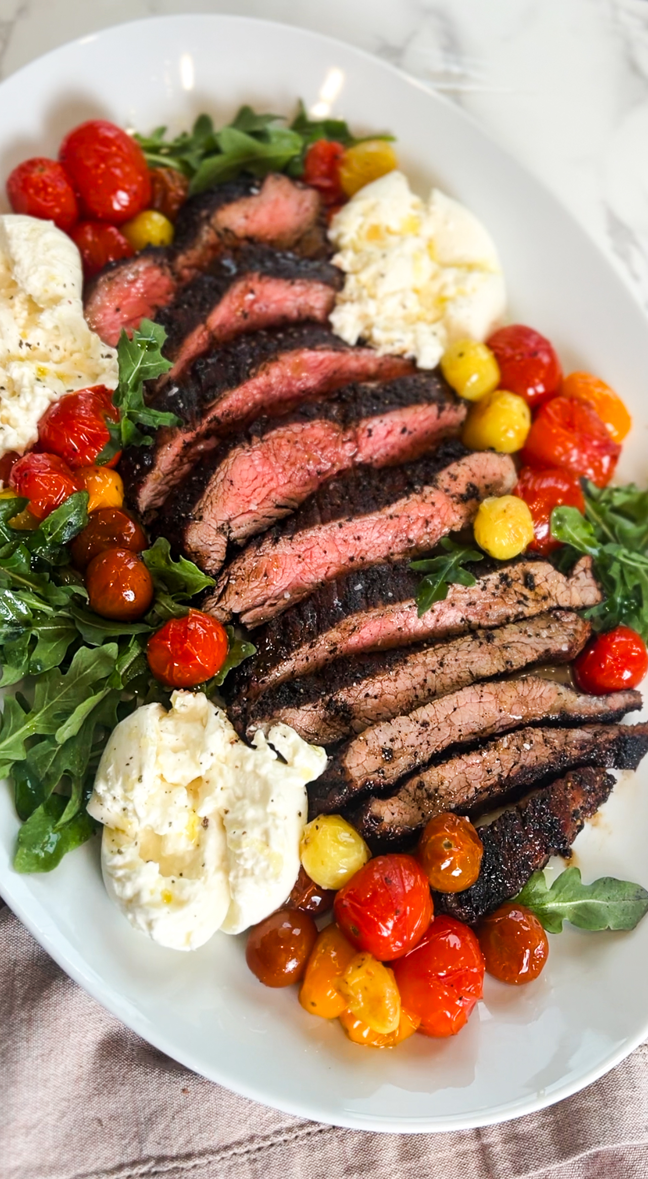 A platter showcasing espresso rub flank steak, cherry tomatoes, arugula, and mozzarella dollops. The medium-rare steak is expertly seasoned with rich coffee notes, surrounded by colorful tomatoes and fresh greens for a vibrant and appetizing presentation.