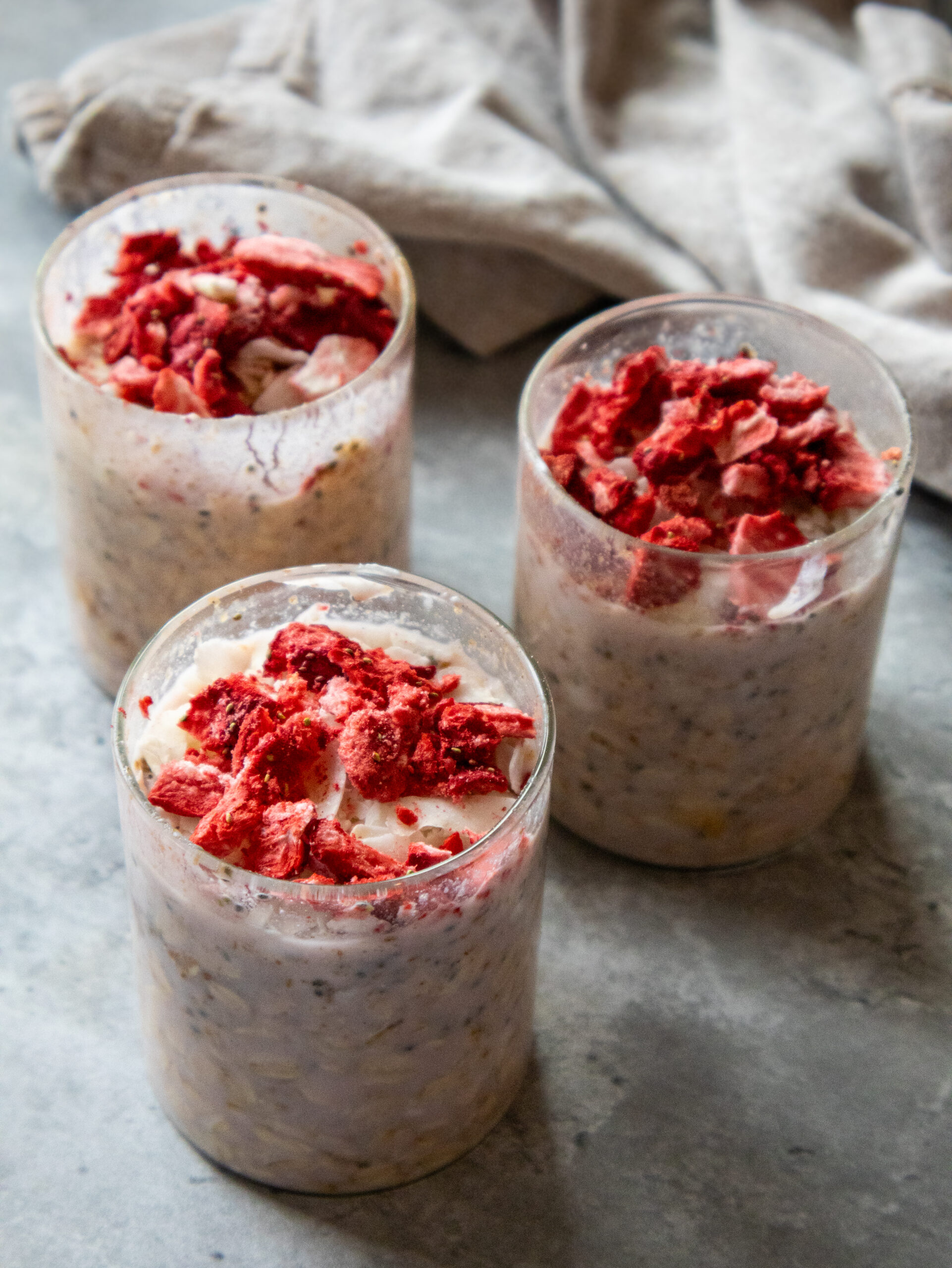 3 overnight oats jars filled with Strawberry Overnight Oats made with strawberry milk topped with strawberries and coconut flakes. 