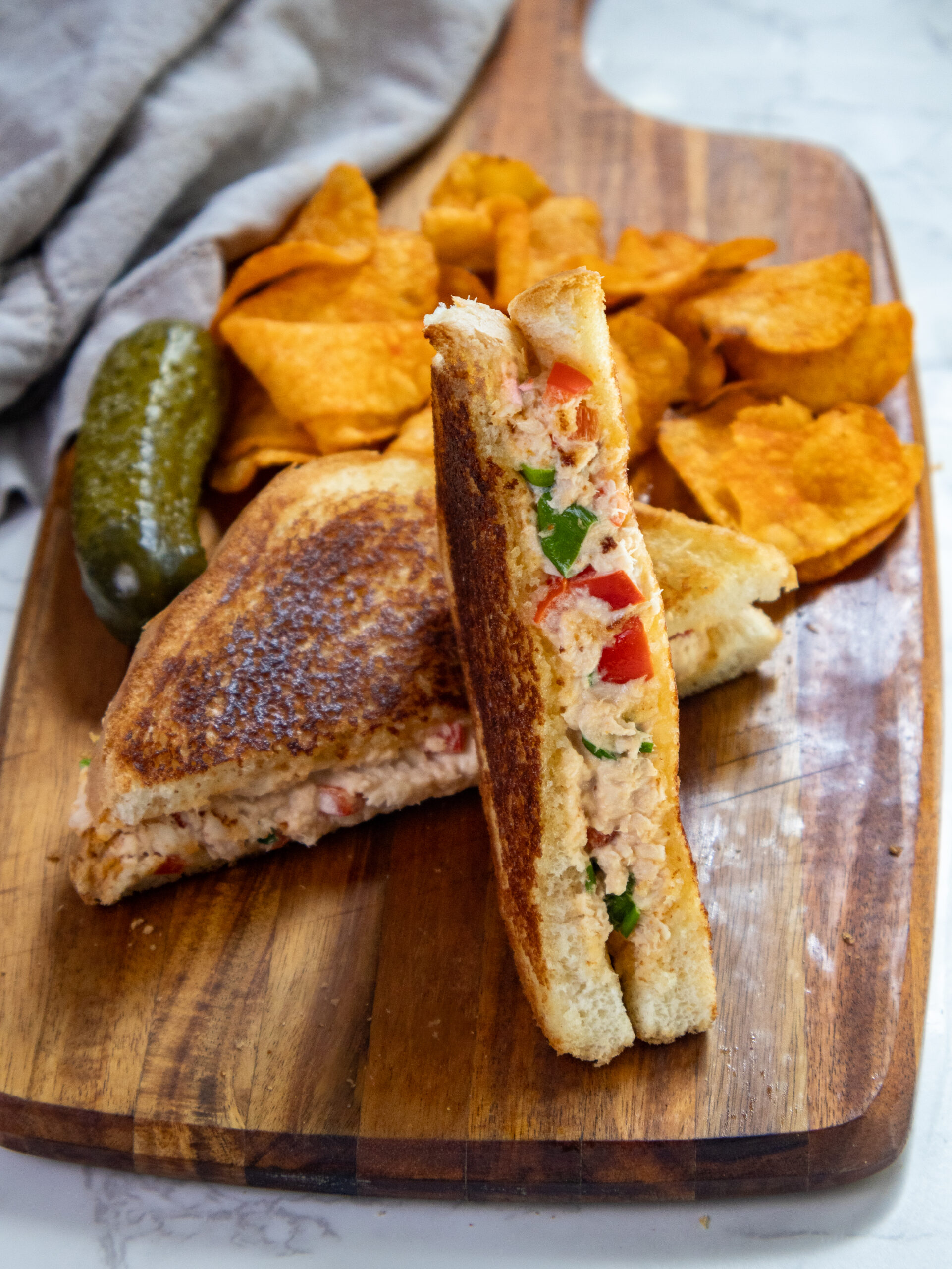 Spicy Asian Style Toasted Tuna Sandwich on a cutting board with chips and a pickle. 