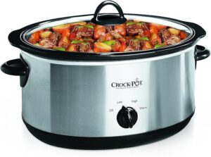 A stainless steel slow cooker filled with a stew of beef chunks, carrots, and green peppers. The cooker features a black lid and handles, with a dial displaying settings for low, high, and warm.